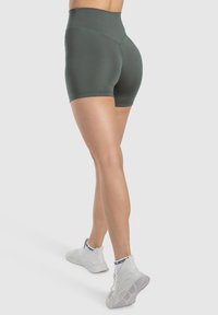 Bermudas de tiro alto en verde oliva con una textura suave, diseño ajustado y un corte a mitad del muslo, combinadas con zapatillas deportivas blancas.