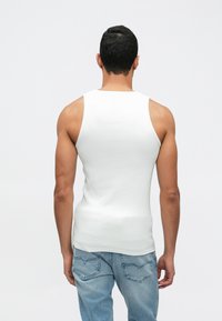 Top de alças branco sem mangas feito de tecido canelado, design justo, combinado com jeans denim azul claro com bolsos traseiros.