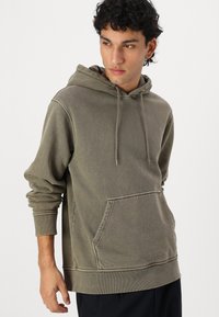 Olivegrüner Hoodie aus weichem Material, mit einer vorderen Kängurutasche, Kapuze mit Kordelzug sowie gerippten Bündchen und Saum.
