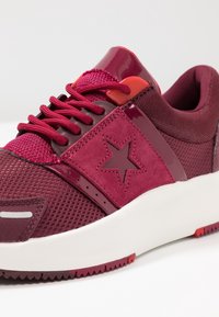 Bordowe sneakersy z siateczki, zamszu i błyszczącymi akcentami. Wyraźne logo gwiazdy z boku, sznurowany design i biała gumowa podeszwa.