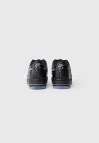 Crne Nike Air tenisice s glatkom kožnom gornjom, teksturiranim naglascima, niskim dizajnom i polu-prozirnim plavim potplatom.