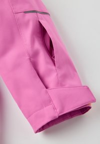 Vaaleanpunaisen takin hiha, jossa on teksturoitu kangas, sivutasku ja kontrastivärinen keltainen vuori hihassa. Heijastava yksityiskohta olkapäällä.