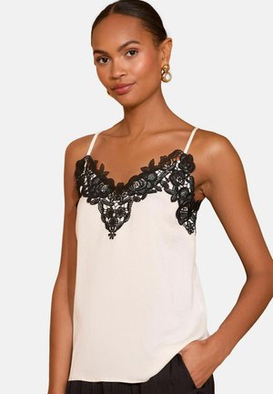 Kätkete puksiga kreemjas tanktopis musta pitsdetailiga kaelaümbruse ääres. Omab õhuke rihmade ja siledat tekstuuri. Rikka lillemustriga kaunistatud.