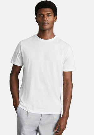 Weißes Baumwoll-T-Shirt mit kurzen Ärmeln, Rundhalsausschnitt und lockerer Passform, kombiniert mit hellgrauen Hosen. Glatte Textur, keine Muster.