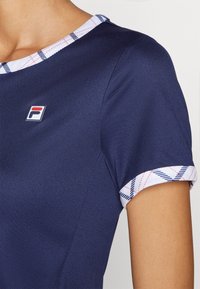 Top atlético azul marino con cuello redondo, con un borde de patrón de cuadros en blanco, rojo y azul. Incluye un pequeño logo en el pecho.