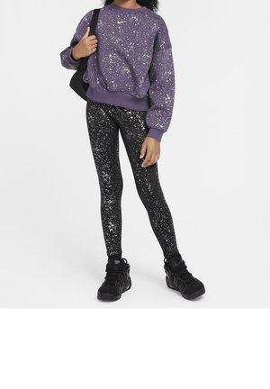 Fioletowa bluza w groszki, czarne legginsy w białe groszki. Czarne sneakersy o teksturowanym wzorze. Modelka trzyma czarną torbę.