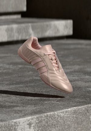 Pantof sport roz pal cu un finisaj lucios, având panouri laterale texturate și o talpă de cauciuc cu model antiderapant. Include șireturi.