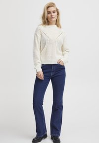 Ivory knitted sweater with a textured pattern, featuring a round neckline and ribbed cuffs, paired with dark blue flared jeans and black boots.