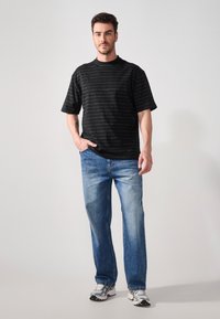 Sort kortærmet t-shirt med hvide vandrette striber, parret med lyseblå straight-leg jeans og grå sneakers.