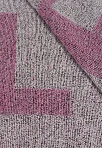 Tappeto d'area texturizzato con un motivo geometrico rosa e grigio. La superficie è intrecciata con fibre visibili, creando una texture morbida e spessa.