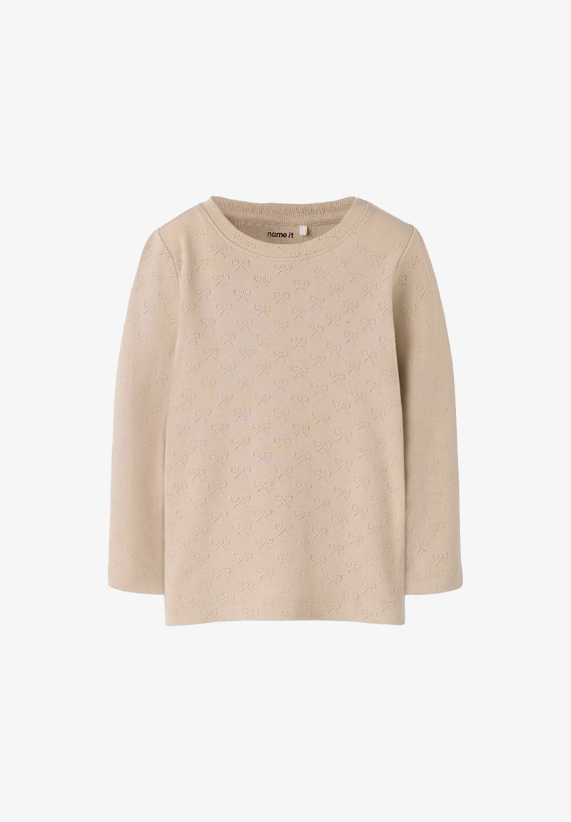 Długi beżowy top z długim rękawem, ozdobiony teksturowanym wzorem drobnych serduszek. Okrągły dekolt, miękki dzianinowy materiał oraz prosty krój bez widocznych zapięć.