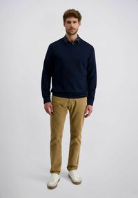 Marineblauer Strickpullover über einem blau-weißen gemusterten Hemd, kombiniert mit khakifarbenen Cordhosen und weißen Sneakers mit beige-farbenen Sohlen.