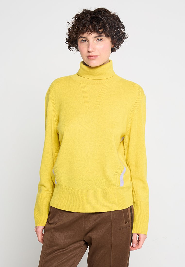 Gelbes Turtleneck-Pullover mit geripptem Muster, ausgestattet mit seitlichen Akzenten in einer helleren Farbe. Kombiniert mit braunen Hosen. Sauberes Design.