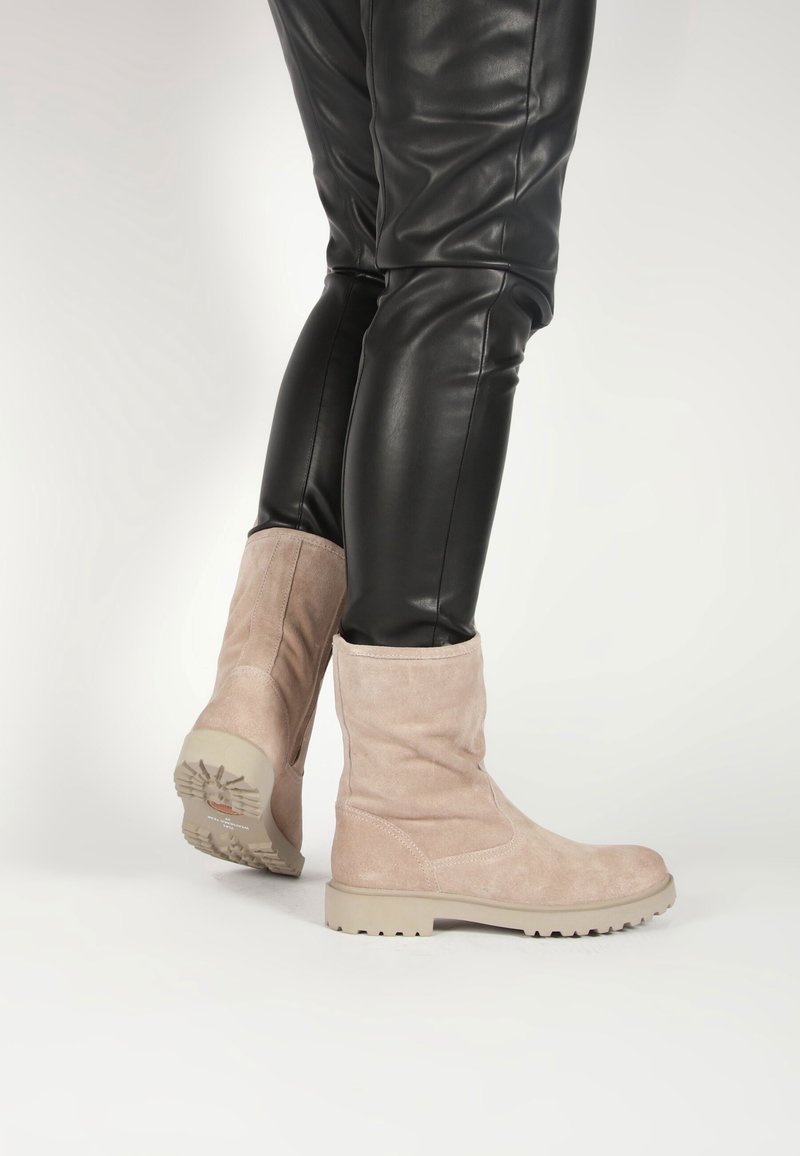 Botines de ante de color beige claro con un diseño sencillo, suelas de goma contrastantes y una textura suave; combinados con pantalones de cuero negros.