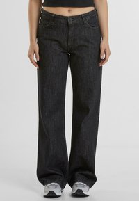Jeans de tiro alto y pierna ancha negros con textura sutil y diseño de cinco bolsillos. Combinados con zapatillas deportivas grises.