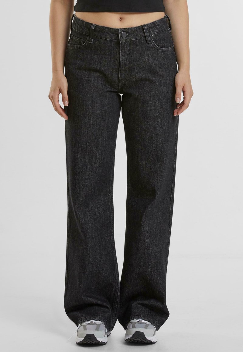 Jeans de tiro alto y pierna ancha negros con textura sutil y diseño de cinco bolsillos. Combinados con zapatillas deportivas grises.