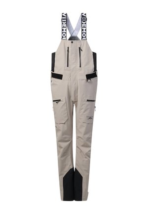 Pantalon salopette imperméable beige clair avec renforts noirs aux genoux, multiples poches zippées et bretelles réglables noires et blanches avec le texte "VIDEMOI".
