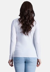 Weißes Langarmhemd aus glattem Stoff, taillierte Passform, von hinten gezeigt mit hellblauen Jeans und welligem, dunklem Haar.