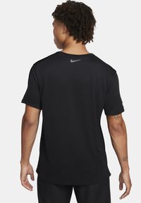 Camiseta deportiva de manga corta negra, hecha de una tela suave. Presenta un diseño elegante con un logo reflectante de Nike en la parte superior de la espalda.