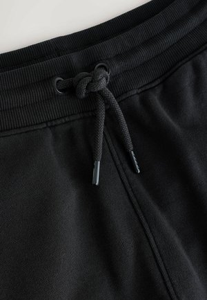 Schwarze Sweathose mit Kordelzug, geripptem Bund, strukturiertem Stoff und geknoteten Kordelzug-Details. Glatte Oberfläche, minimalistisches Design.