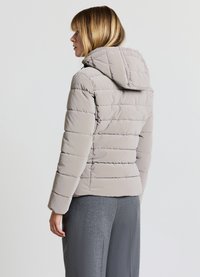 Giacca a vento grigio chiaro con cappuccio, caratterizzata da un design trapuntato e cuciture orizzontali. Tessuto morbido e silhouette aderente.