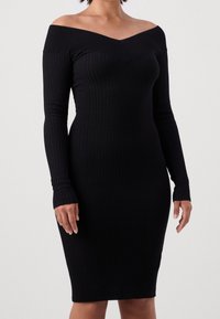 Abito nero a costine con design off-shoulder, maniche lunghe e silhouette aderente, caratterizzato da scollatura a V e texture a costine.