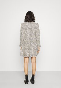 Mönstrad klänning med långa ärmar, samlad midja och utsvängd kjol, med en svart och krämfärgad design. Bärs med svarta ankelboots.