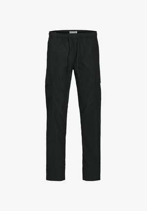 Teen dreng går, iført en blå pufferjakke med hætte, sorte cargo-bukser og beige støvler mod en ensfarvet lys baggrund.