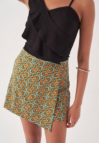 Haut noir texturé avec détail à volants ; mini-jupe vibrante présentant un motif géométrique en orange, vert et bleu clair ; ourlet asymétrique.