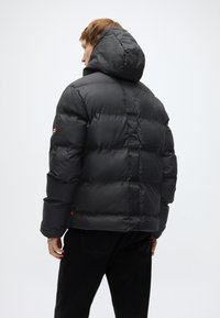 Μαύρο κοντό μπουφάν με κουκούλα, σχεδιασμό με ραφές και λεία, λαμπερή υφή. Διαθέτει κόκκινη λεπτομέρεια στο μανίκι και κάθετη ραφή στην πλάτη.