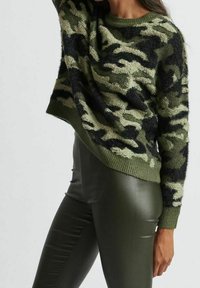 Grön kamouflagemönstrad tröja med en fuzzy textur, rund halsringning och avslappnad passform, kombinerad med glänsande mörkgröna leggings.