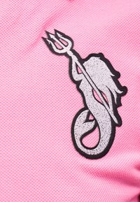 Λευκή κεντημένη γοργόνα που κρατά τρίαινα σε υφασμένη ροζ υφή, με μαύρο περίγραμμα.