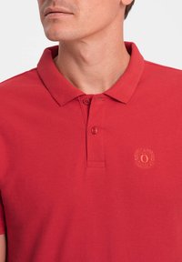 T-shirt polo rouge avec un tissu texturé, des manches courtes, une patte de boutonnage et un logo brodé sur la poitrine gauche.