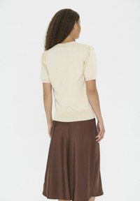 Beige short-sleeve sweater with subtle texture, paired with a knee-length brown skirt, shown from the back. Soft, fitted, and relaxed design.