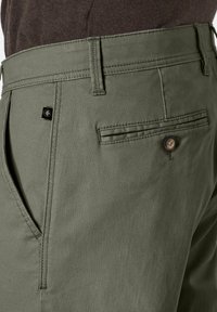 Olivgrüne Hosen aus strukturiertem Stoff, mit einer Gesäßtasche mit Knopf und einem kleinen Logoetikett nahe dem Bund.