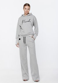 Szary hoodie z czarnym odręcznym logo, zestawiony z luźnymi szarymi spodniami z boczną kieszenią i czarnym sznurkiem.