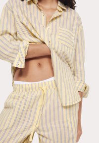 Geel gestreepte shirt met knoopsluiting en borstzak, gecombineerd met bijpassende gestreepte broek met een elastische tailleband en trekkoord.