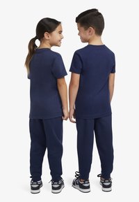 Completo in cotone blu navy composto da t-shirt a maniche corte e pantaloni della tuta con elastico in vita, abbinato a scarpe da ginnastica bianche e nere.