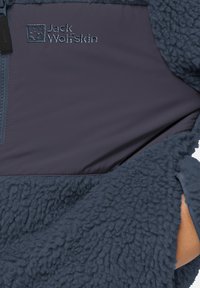 Jack Wolfskin Fleecejacke mit einer dunkelblauen strukturierten Außenseite, glatten Einsätzen, Reißverschluss und gesticktem Logo.