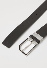 Cintura in pelle nera con texture, dotata di una fibbia rettangolare argentata con il nome del marchio, include diversi fori per la regolazione.