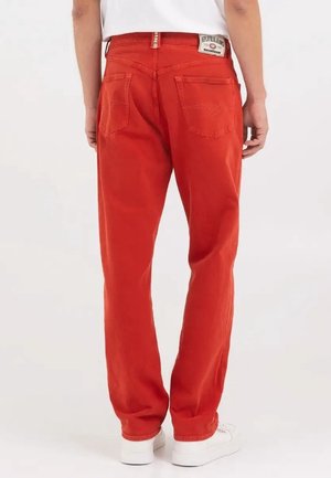 Person trägt rote Jeans mit geradem Bein und Gesäßtaschen, kombiniert mit weißen Sneakers und weißem Oberteil, von hinten gezeigt.