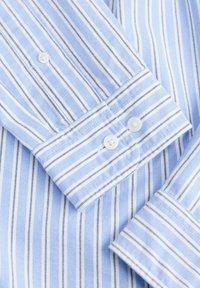 Manches de chemise bleu clair avec des rayures verticales blanches et bleu marine, avec des poignets boutonnés avec des boutons blancs.
