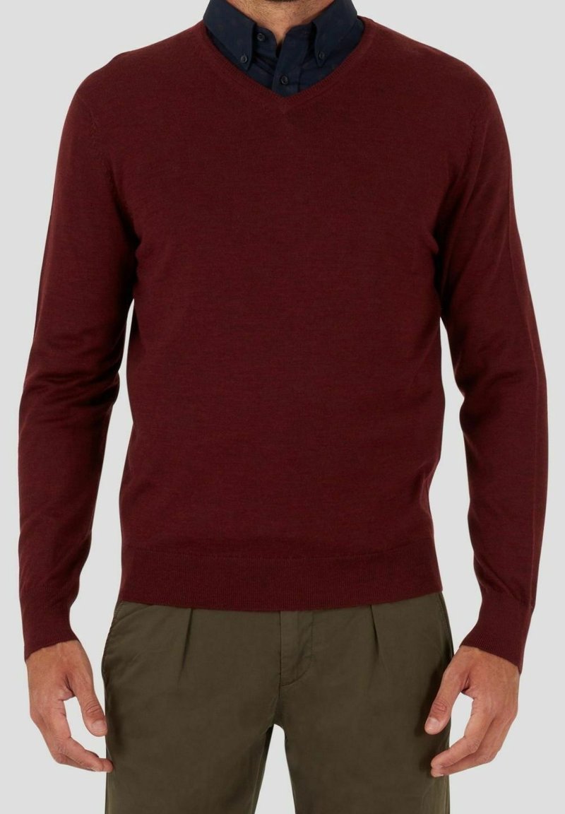 Burgunderfarbener V-Ausschnitt-Pullover aus Strickstoff, mit langen Ärmeln und schmaler Passform, kombiniert mit einem dunkelblauen Hemd darunter.