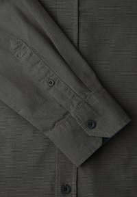 Dunkelgrauer Hemdsärmel und Manschette mit schwarzen Knöpfen und feiner strukturierter Stoffstruktur, die aus der Nahaufnahme sichtbar ist.