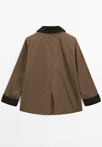 Giacca marrone con colletto in velluto a coste, maniche lunghe con polsini scuri e uno spacco posteriore per facilitare i movimenti. Il tessuto presenta una texture liscia.