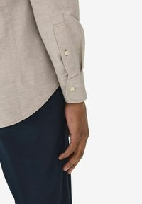 Ljusbeige skjorta med långa ärmar, som har knäppta manschetter och en jämn textur, ihop med marinblå byxor.