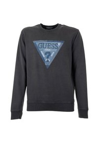 Felpa nera con una toppa triangolare in denim blu che presenta il marchio "GUESS" e del testo. Collo e polsini a costine, design casual.