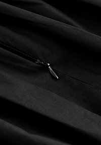 Tessuto nero con una superficie liscia e una zip visibile. La zip presenta un cursore metallico che si fonde delicatamente con il materiale scuro.