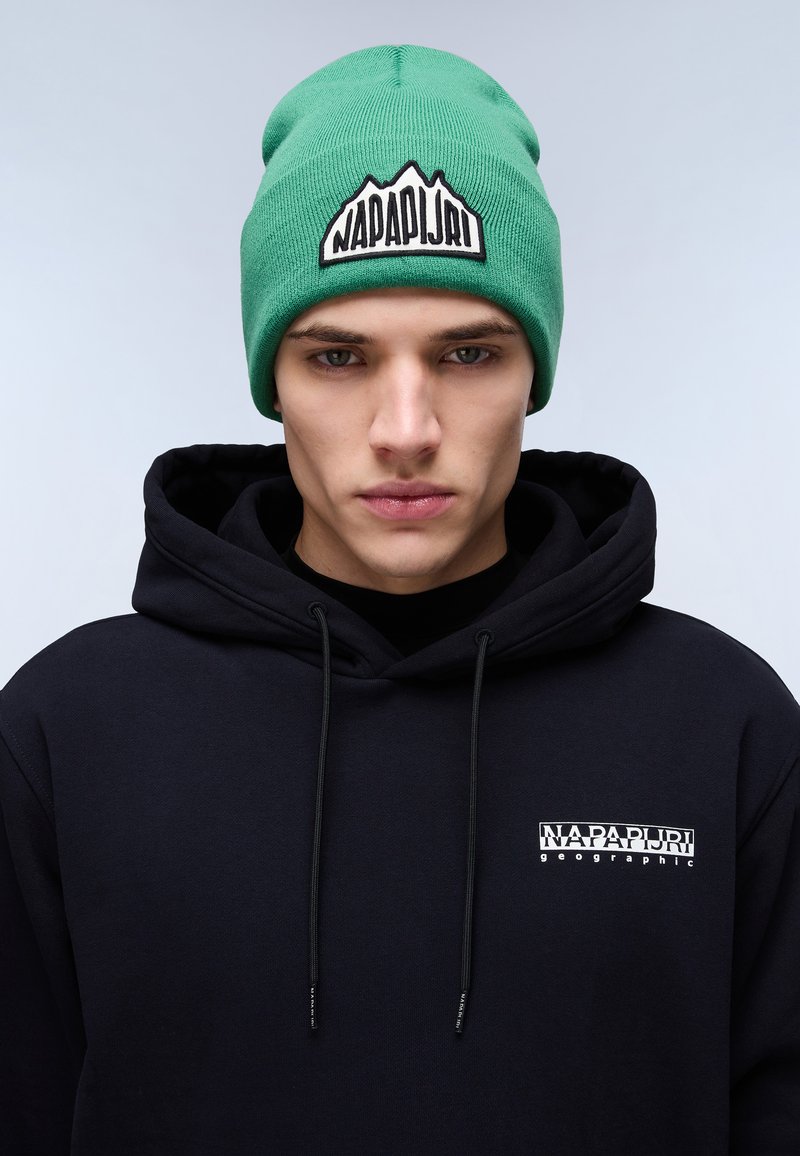 Berretto a maglia verde con un logo di montagna e testo ricamato in nero; abbinato a una felpa con cappuccio nera con un piccolo logo sul petto.
