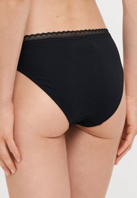 Zwarte hooghangende onderbroek met een kanten rand langs de tailleband. Gemaakt van zachte, rekbare stof voor optimaal comfort.